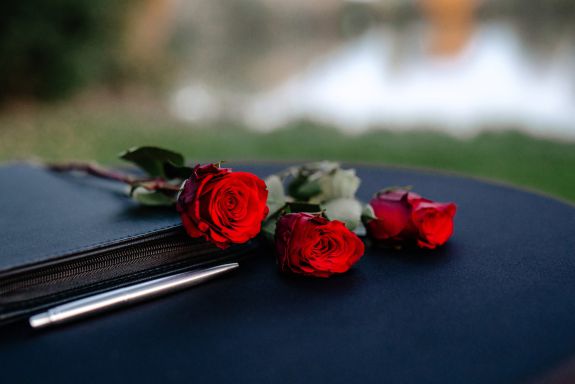 drei rote Rosen liegen auf einem schwarzen Tisch mit einem schwarzen Buch